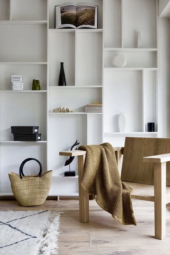 Modern white minimalist bookshelf with geometric compartments styled with decor, natural wood chair and woven basket
