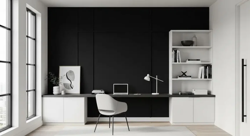 Minimalist modern home office with a black accent wall, white desk, ergonomic mesh chair, and a single floating shelf in bright natural light