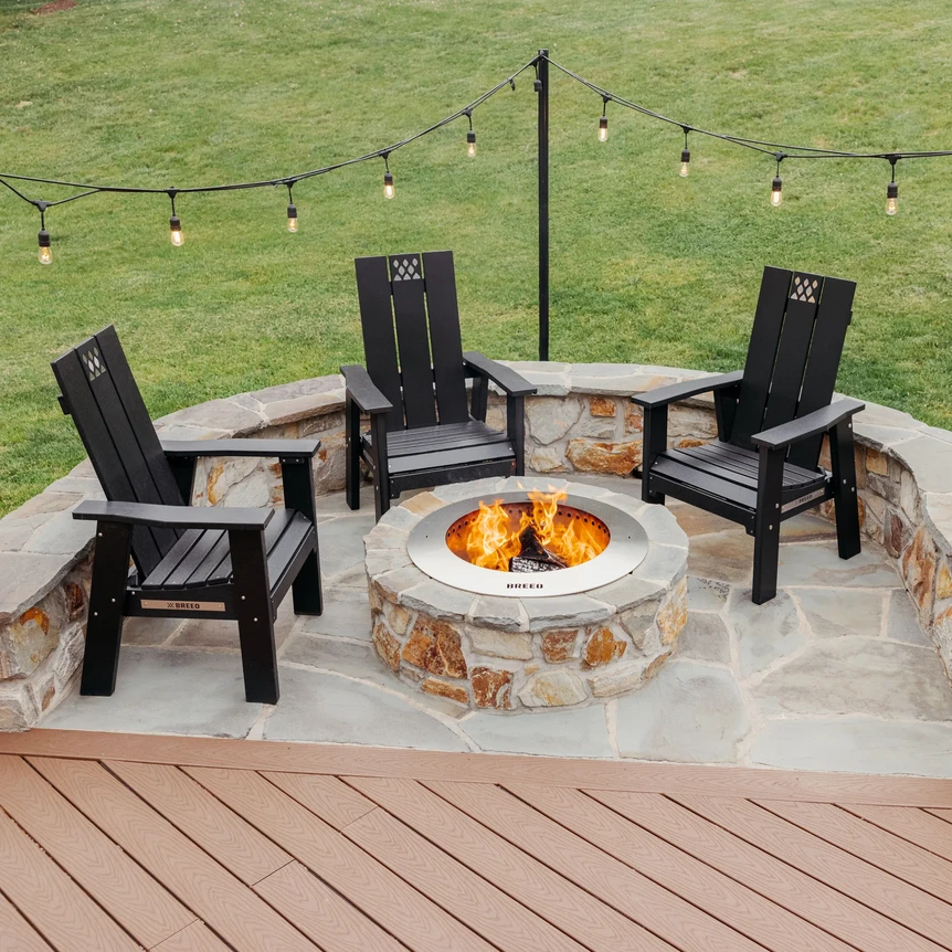 Outdoor fire pit patio with four black Adirondack chairs on stone pavers and string lights overhead