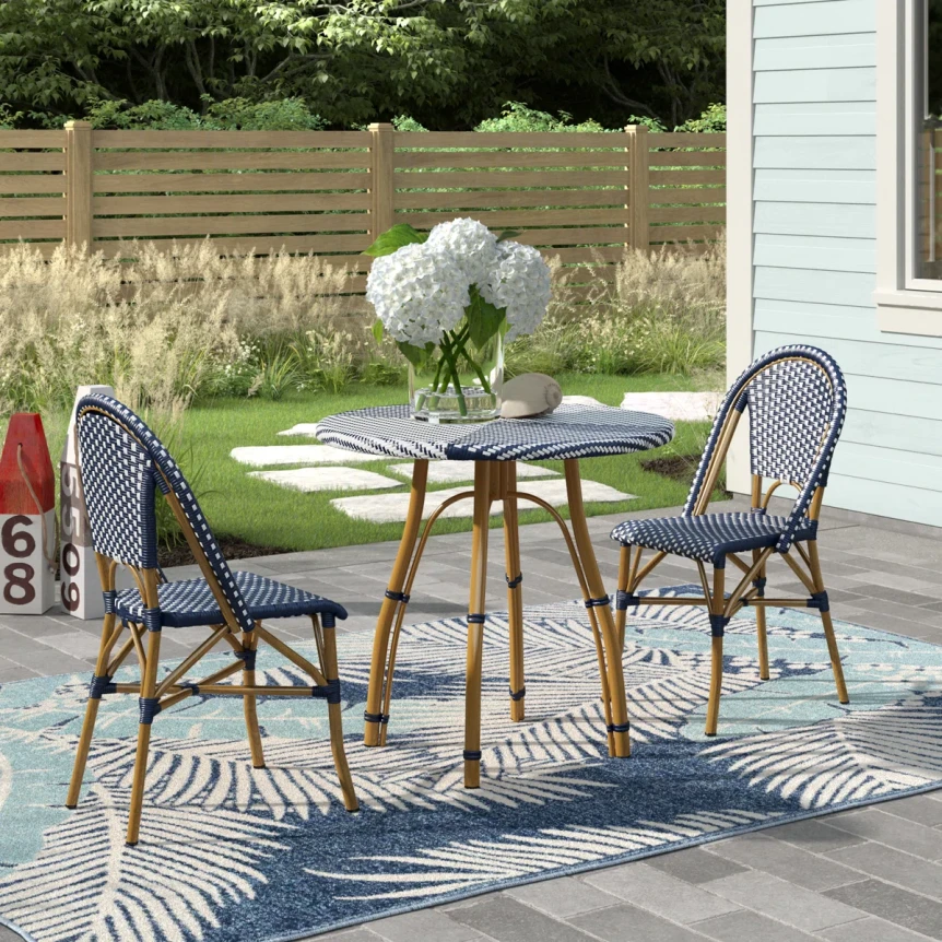 Modern patio bistro set with round glass table and navy woven chairs on striped outdoor rug