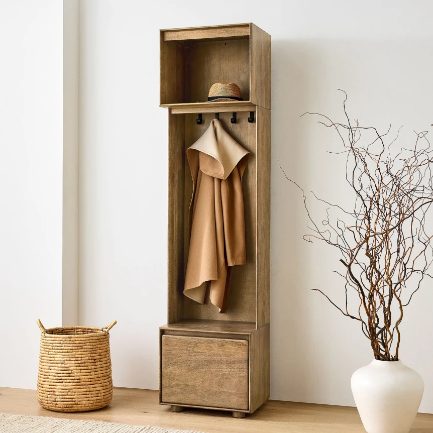 Wooden hall tree with coat hooks, storage compartment, and drawer beside woven basket and decorative branches
