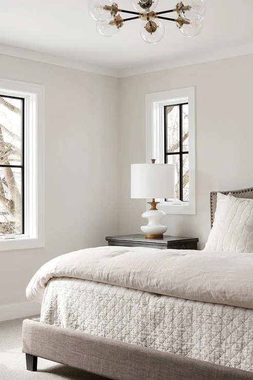 Modern minimalist bedroom with white walls, natural light from black-framed windows, and neutral bedding