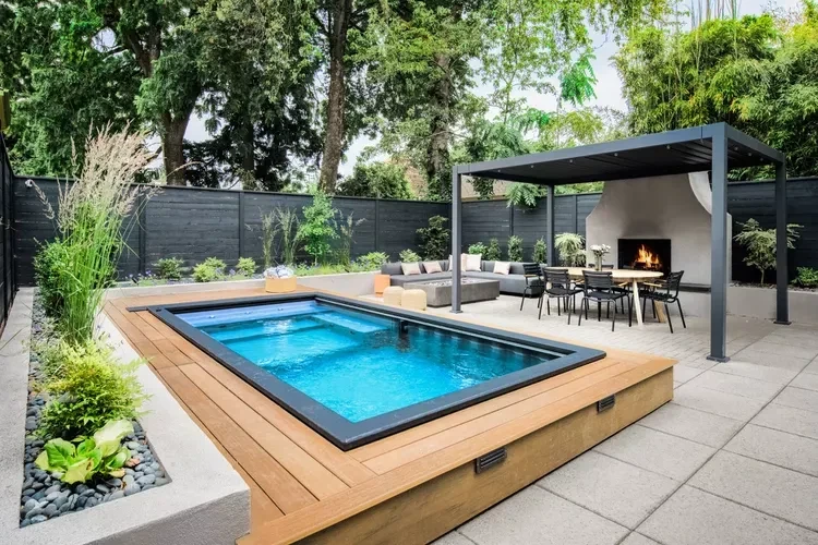 Modern backyard with raised wooden deck pool, outdoor kitchen pavilion, and landscaped garden with patio seating