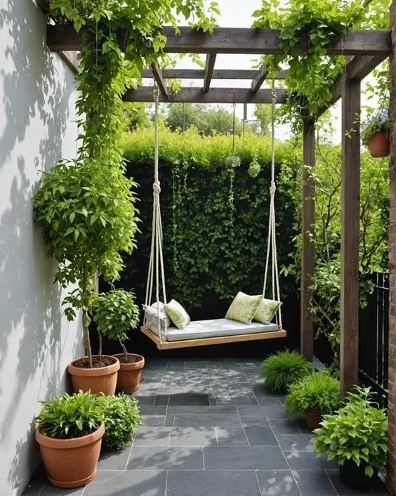 Tranquil patio corner with wooden swing, pergola, potted plants, and lush green privacy hedges creating peaceful outdoor s...
