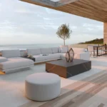 Modern outdoor living space with minimalist furniture, wooden deck, and seamless ocean views under covered patio