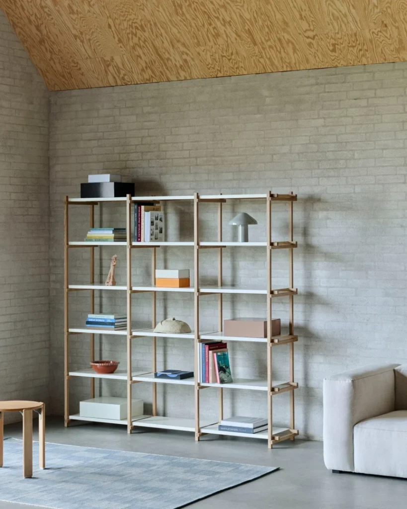 Modern minimalist bookshelf with light wood frame and white shelves displaying books and decor against concrete wall
