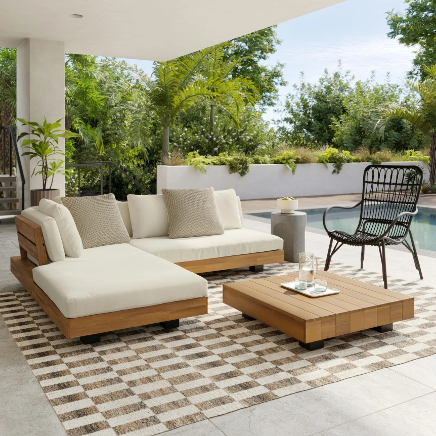 Modern outdoor patio with white cushioned sectional sofa, wooden coffee tables, and woven accent chair on geometric rug