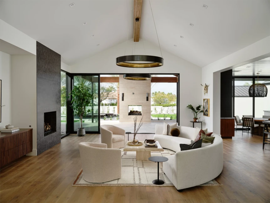 Modern living room with vaulted ceiling, large glass doors connecting to outdoor patio, curved sofa, and wood floors