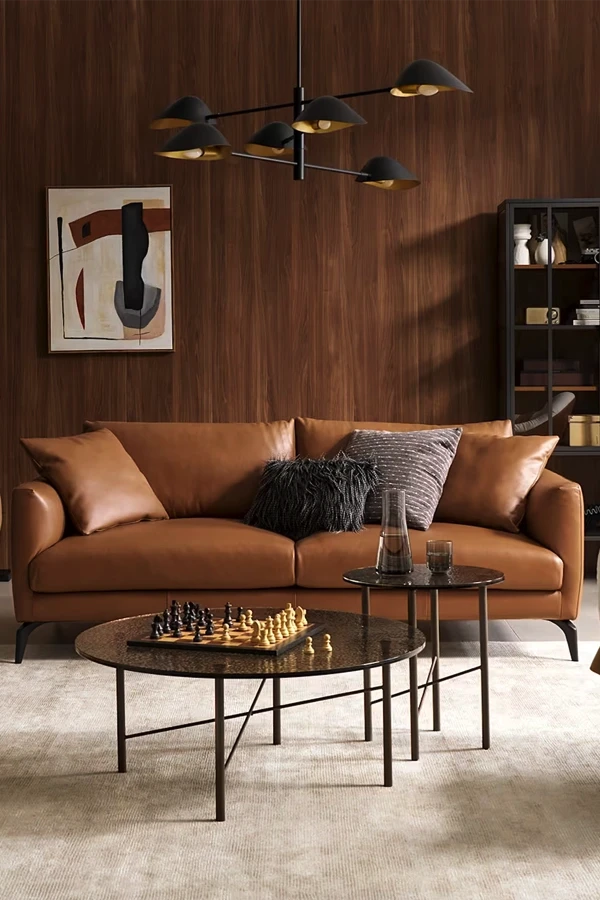Modern living room with tan leather sofa, round coffee tables, and warm wood paneling