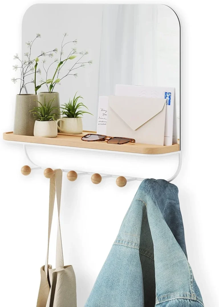 Wall-mounted mirror with wooden shelf and coat hooks holding bags and denim jacket in entryway