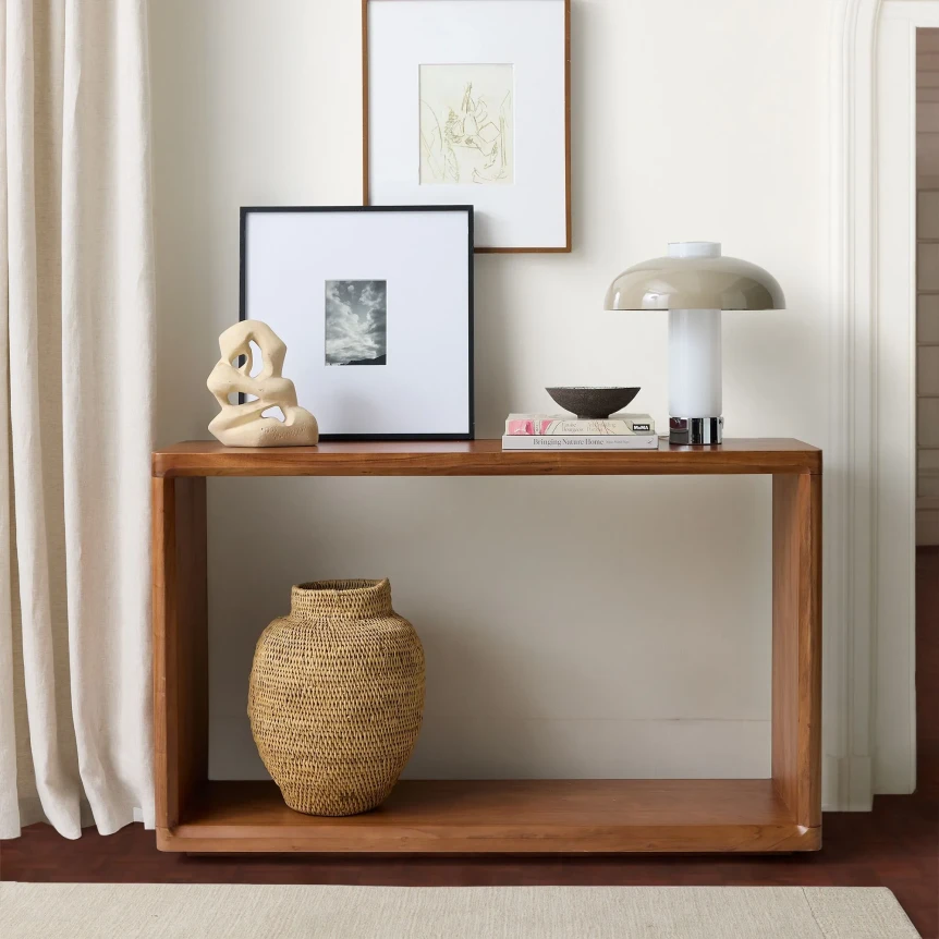 Modern wooden console table with decorative vase, lamp, and framed artwork in minimalist entryway setting