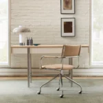 Minimalist wooden desk with metal legs paired with modern tan office chair in bright room with white brick wall