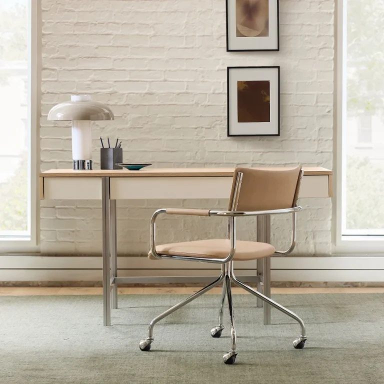 Minimalist wooden desk with metal legs paired with modern tan office chair in bright room with white brick wall