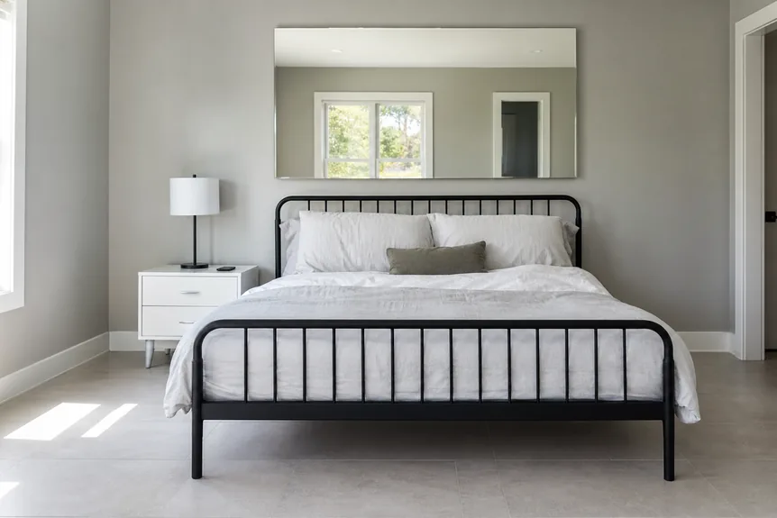 Black metal framed bed with white bedding in minimalist modern bedroom with grey walls and tiled floor
