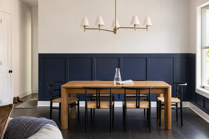 Navy blue wainscoting wall panels in modern dining room with natural wood table and black chairs